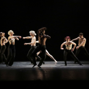 Modern dancers in black pants and bare chest on stage performing.