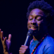 A singer holds a microphone and gestures upward onstage.