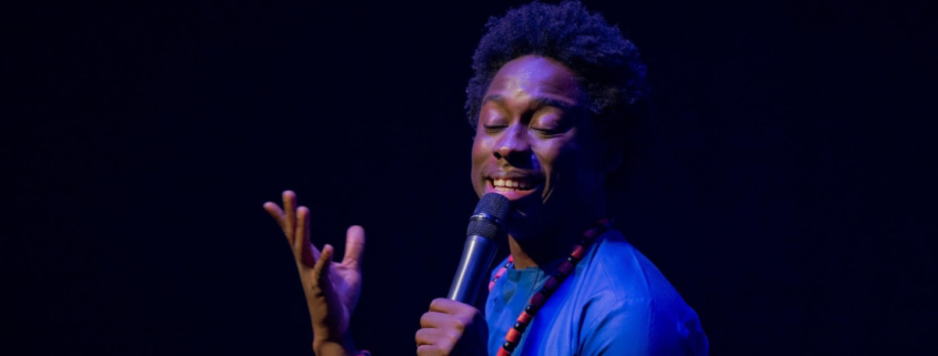 A singer holds a microphone and gestures upward onstage.